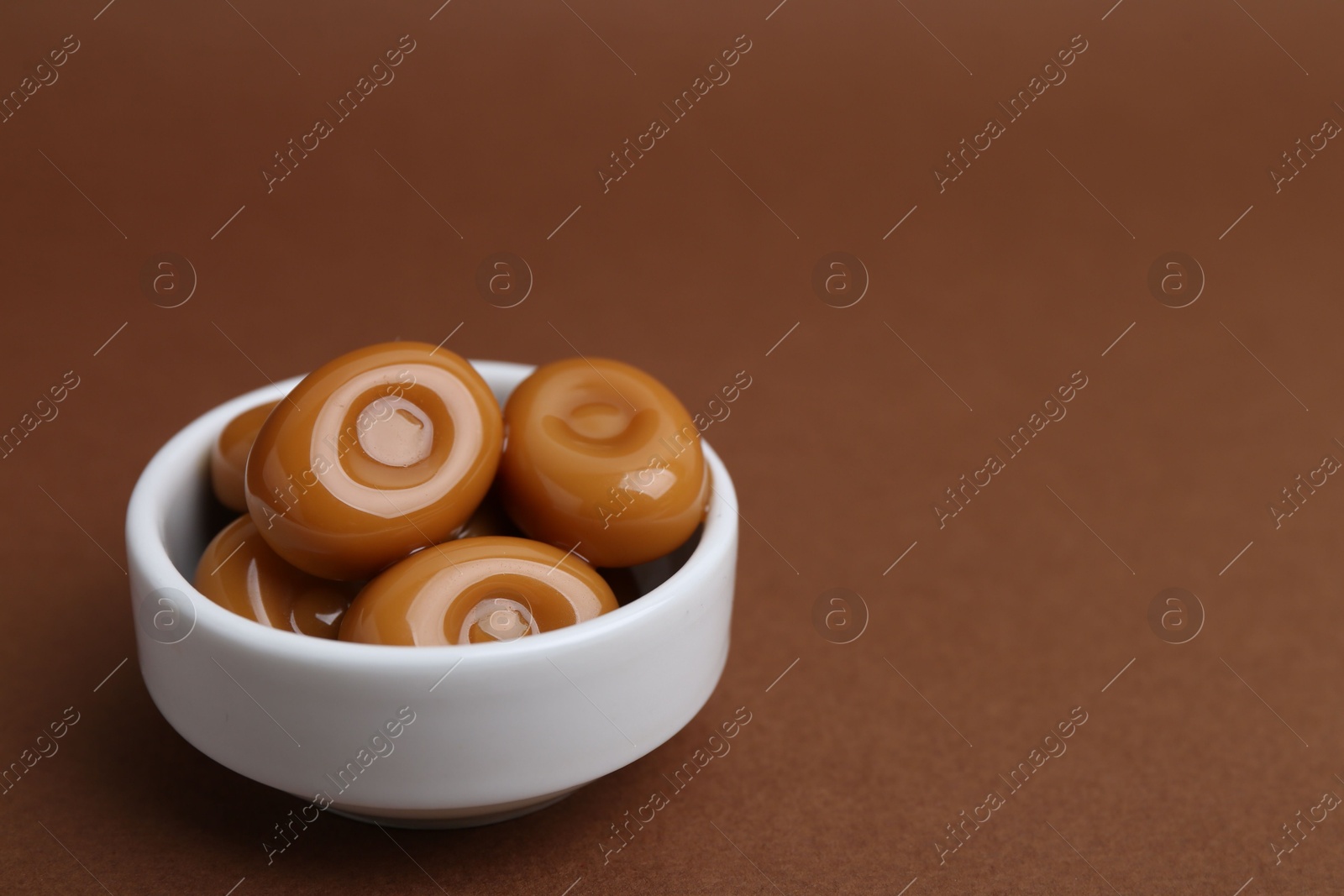 Tasty sweet caramel candies on brown background, closeup. Space for text Photo of Tasty sweet caramel candies on brown background, closeup. Space for text