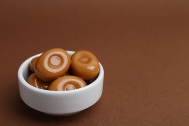 Photo of Tasty sweet caramel candies on brown background, closeup. Space for text