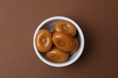 Photo of Tasty sweet caramel candies on brown background, top view