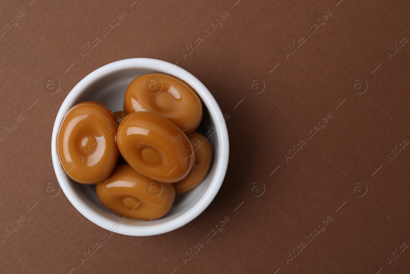 Tasty sweet caramel candies on brown background, top view. Space for text Photo of Tasty sweet caramel candies on brown background, top view. Space for text