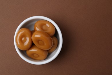 Photo of Tasty sweet caramel candies on brown background, top view. Space for text
