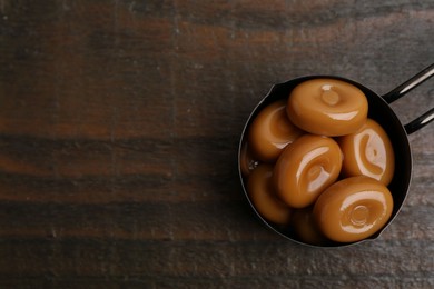 Photo of Tasty sweet caramel candies on wooden table, top view. Space for text