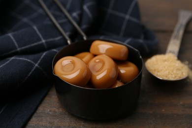 Photo of Tasty sweet caramel candies and sugar on wooden table, closeup