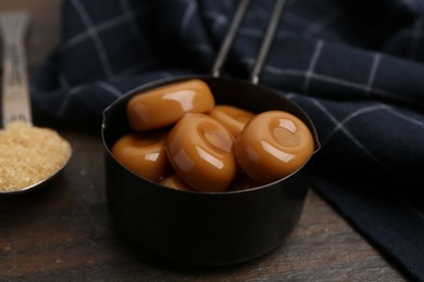 Photo of Tasty sweet caramel candies and sugar on wooden table, closeup