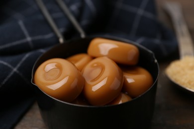 Photo of Tasty sweet caramel candies and sugar on wooden table, closeup