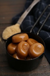Photo of Tasty sweet caramel candies and sugar on wooden table, closeup