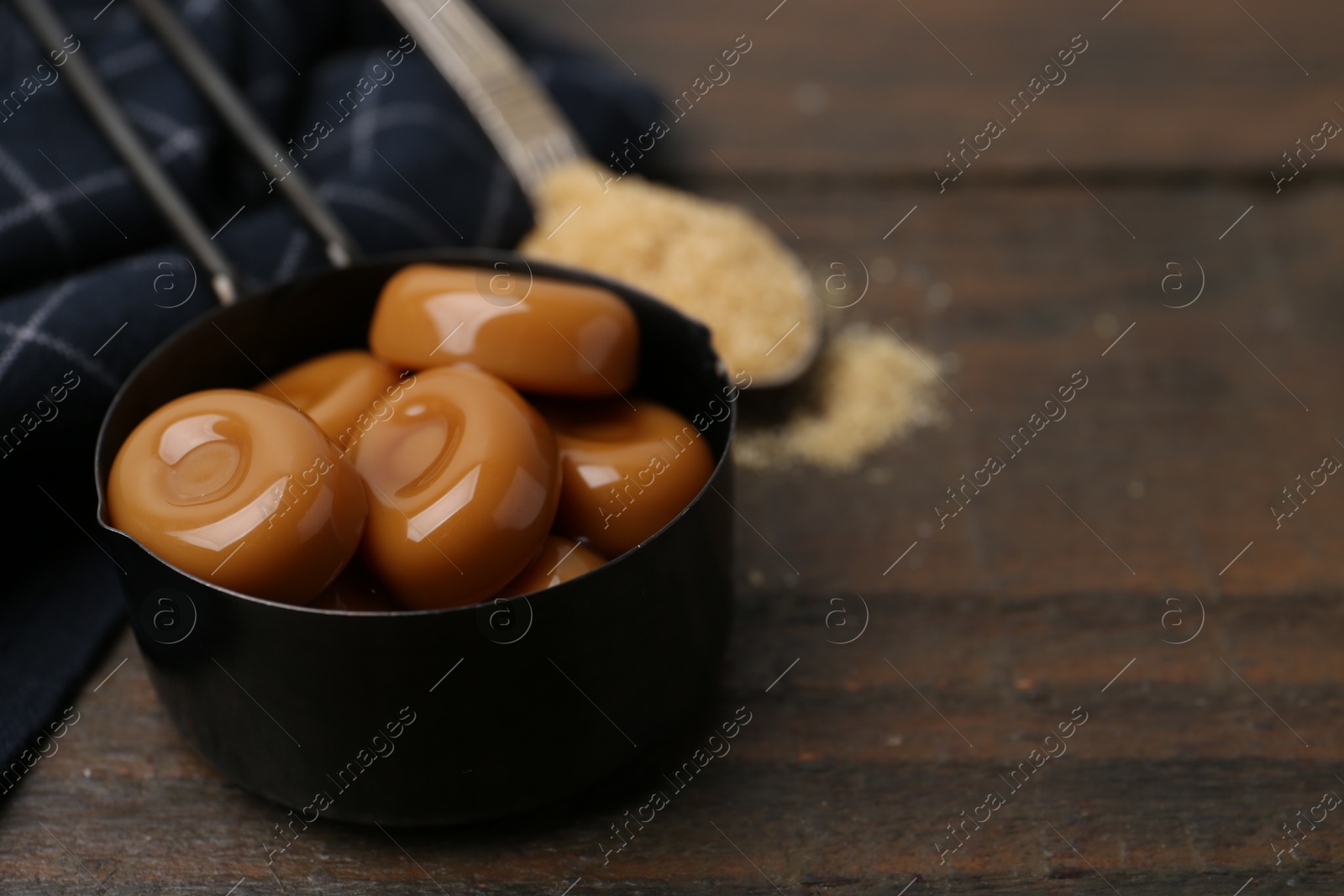 Tasty sweet caramel candies and sugar on wooden table, closeup. Space for text Photo of Tasty sweet caramel candies and sugar on wooden table, closeup. Space for text