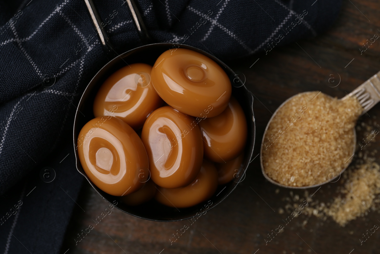Tasty sweet caramel candies and sugar on wooden table, top view Photo of Tasty sweet caramel candies and sugar on wooden table, top view