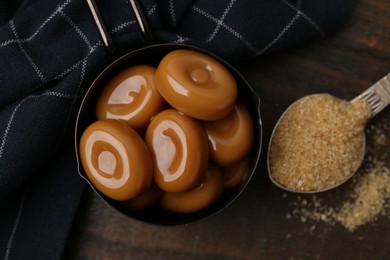 Photo of Tasty sweet caramel candies and sugar on wooden table, top view
