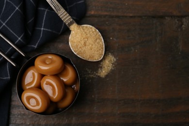 Photo of Tasty sweet caramel candies and sugar on wooden table, top view. Space for text