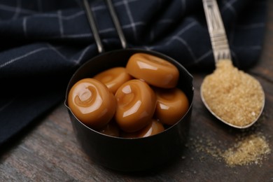 Photo of Tasty sweet caramel candies and sugar on wooden table, closeup