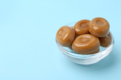 Photo of Tasty sweet caramel candies on light blue background, closeup. Space for text