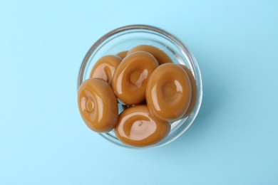 Photo of Tasty sweet caramel candies on light blue background, top view