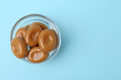 Photo of Tasty sweet caramel candies on light blue background, top view. Space for text