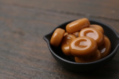 Photo of Tasty sweet caramel candies on wooden table, closeup. Space for text