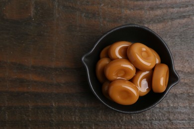 Photo of Tasty sweet caramel candies on wooden table, top view. Space for text