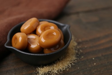 Photo of Tasty sweet caramel candies on wooden table, closeup. Space for text