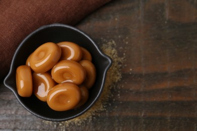 Photo of Tasty sweet caramel candies on wooden table, top view. Space for text