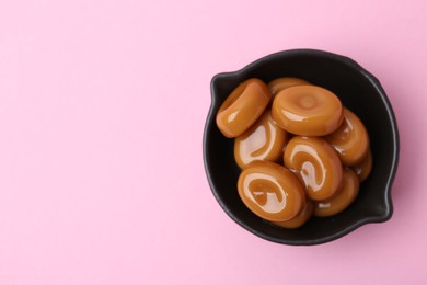 Photo of Tasty sweet caramel candies on pink background, top view. Space for text