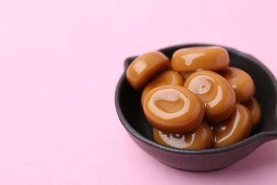 Photo of Tasty sweet caramel candies on pink background, closeup. Space for text