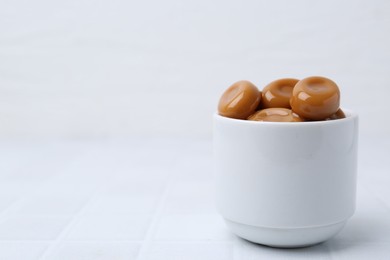 Photo of Tasty sweet caramel candies on white tiled table, closeup. Space for text