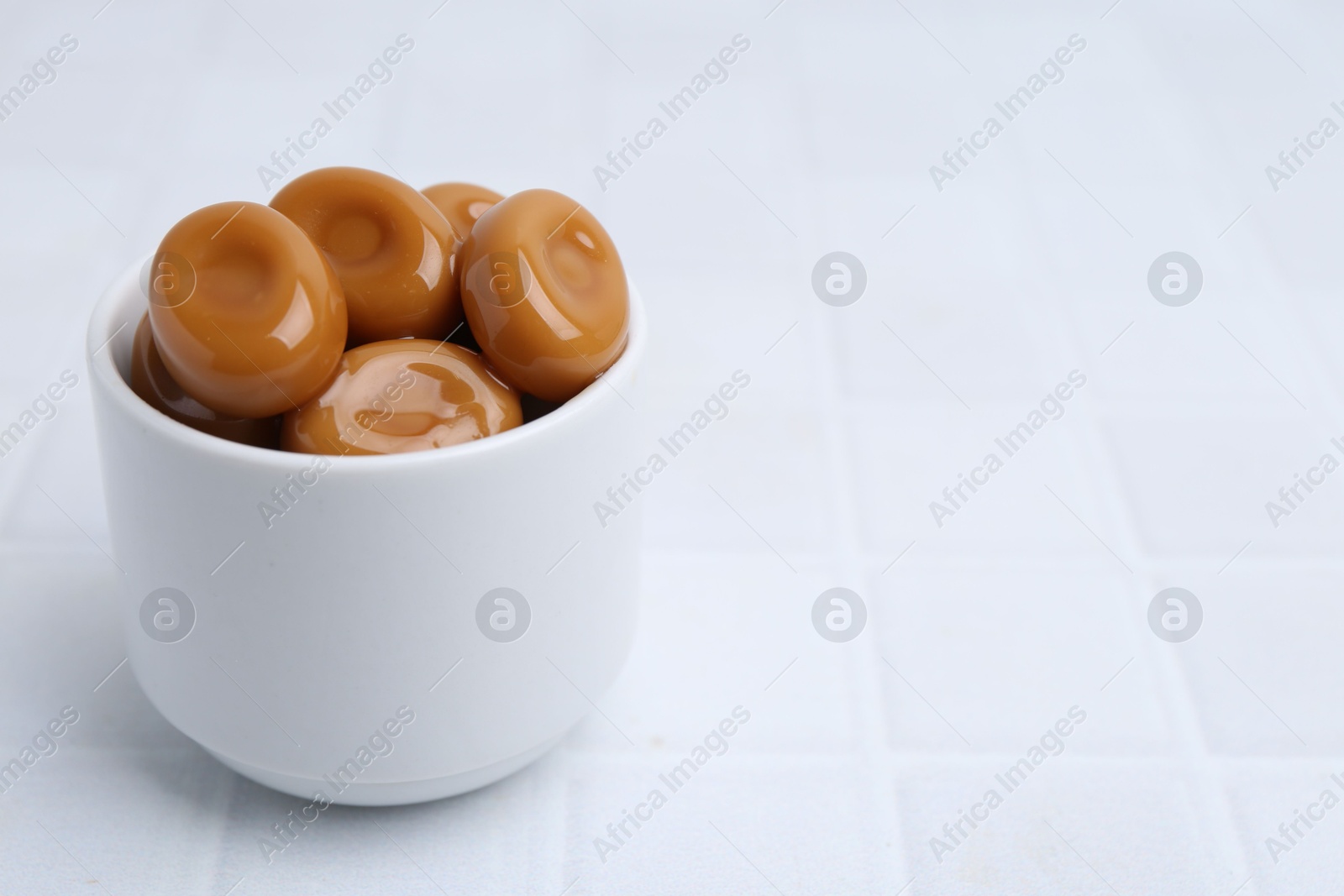 Tasty sweet caramel candies on white tiled table, closeup. Space for text Photo of Tasty sweet caramel candies on white tiled table, closeup. Space for text