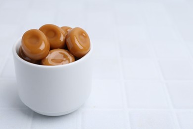 Photo of Tasty sweet caramel candies on white tiled table, closeup. Space for text