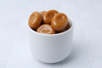 Photo of Tasty sweet caramel candies on white tiled table, closeup