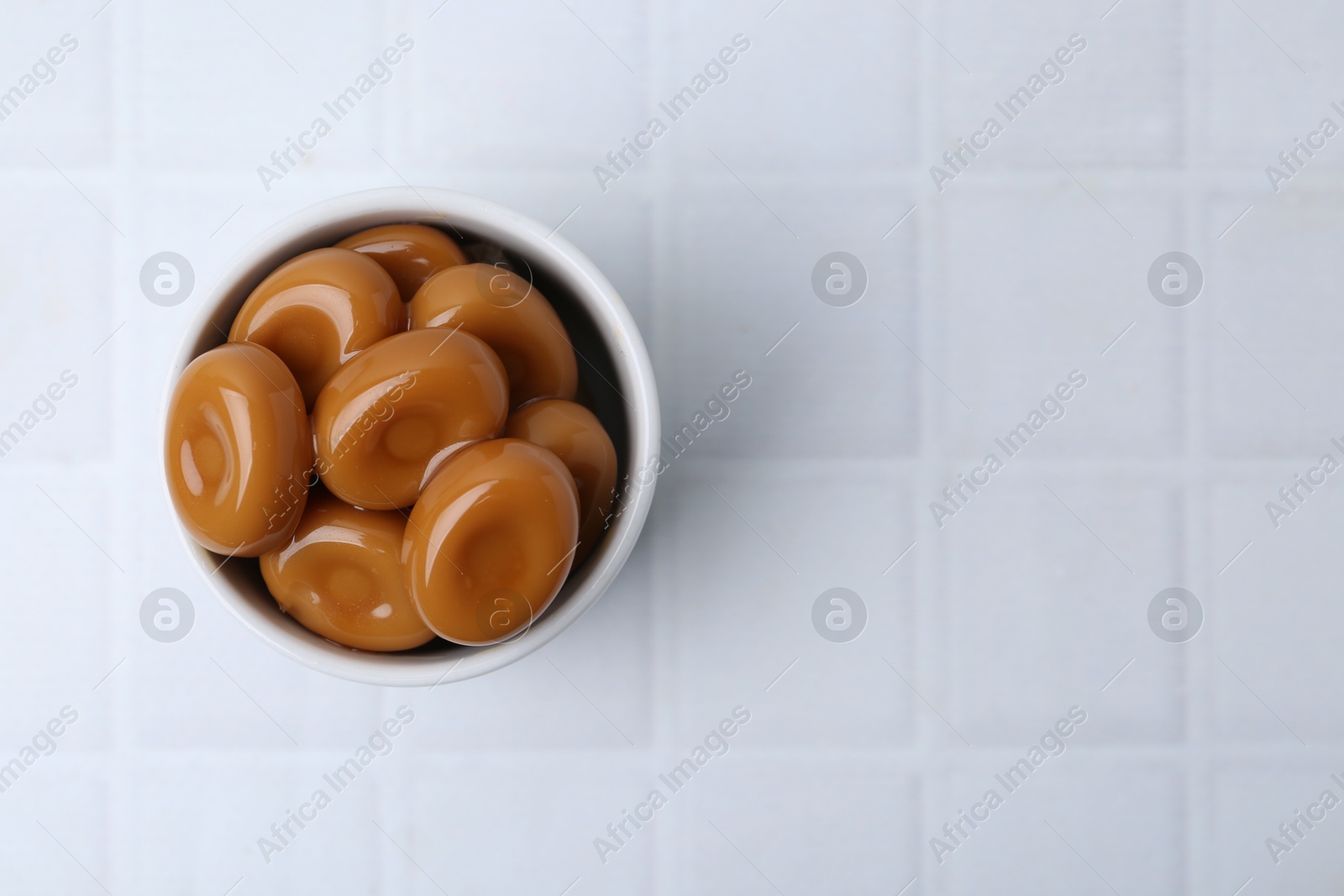 Tasty sweet caramel candies on white tiled table, top view. Space for text Photo of Tasty sweet caramel candies on white tiled table, top view. Space for text