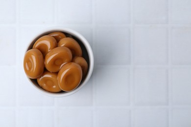 Photo of Tasty sweet caramel candies on white tiled table, top view. Space for text