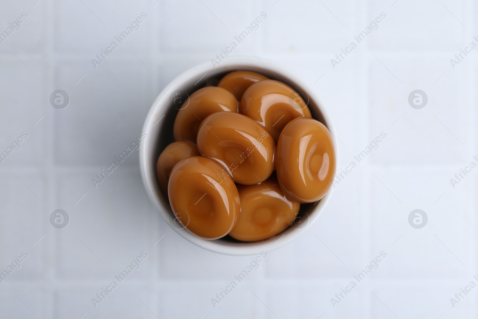 Tasty sweet caramel candies on white tiled table, top view Photo of Tasty sweet caramel candies on white tiled table, top view