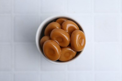 Photo of Tasty sweet caramel candies on white tiled table, top view