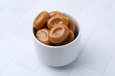 Photo of Tasty sweet caramel candies on white tiled table, closeup