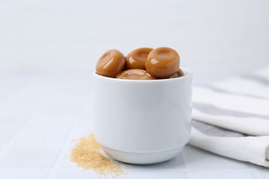 Photo of Tasty sweet caramel candies on white tiled table, closeup