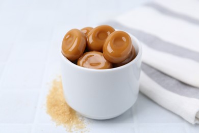 Photo of Tasty sweet caramel candies on white tiled table, closeup