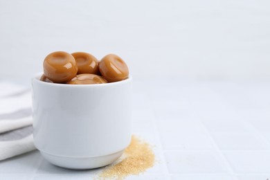 Photo of Tasty sweet caramel candies on white tiled table, closeup. Space for text