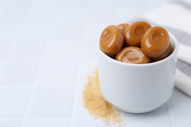 Photo of Tasty sweet caramel candies on white tiled table, closeup. Space for text