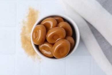 Photo of Tasty sweet caramel candies on white tiled table, top view