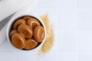 Photo of Tasty sweet caramel candies on white tiled table, top view. Space for text