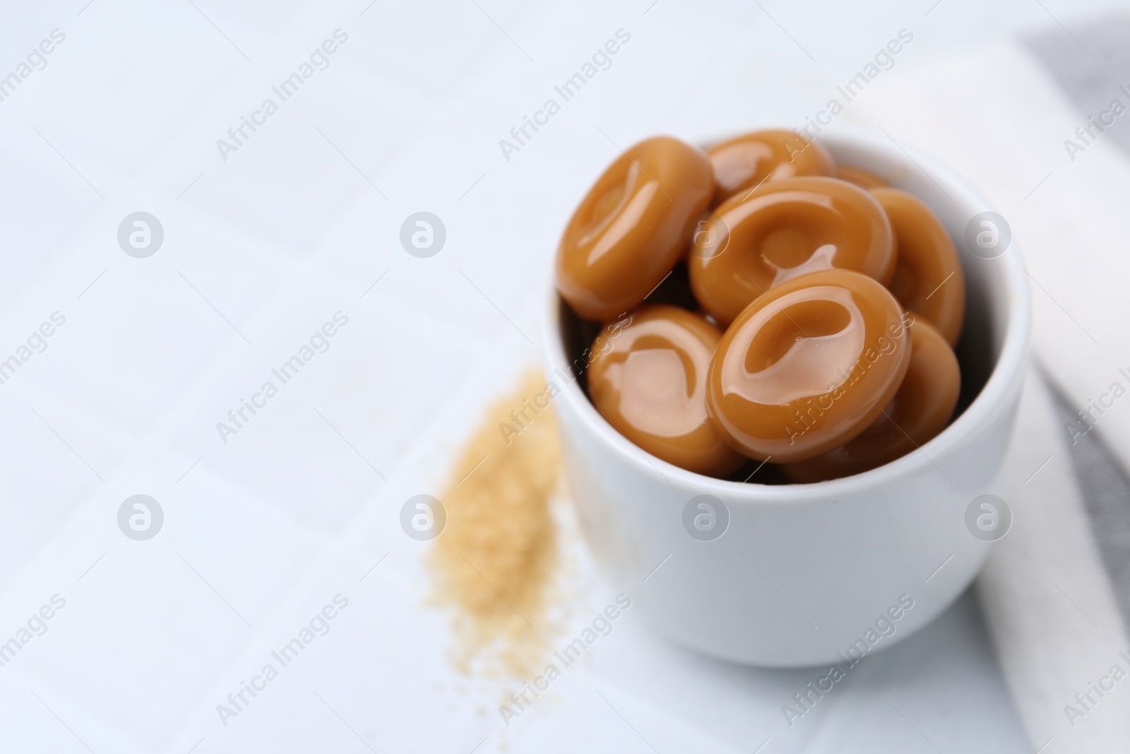 Tasty sweet caramel candies on white tiled table, closeup. Space for text Photo of Tasty sweet caramel candies on white tiled table, closeup. Space for text