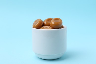 Photo of Tasty sweet caramel candies on light blue background, closeup