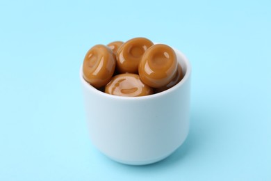 Photo of Tasty sweet caramel candies on light blue background, closeup