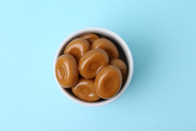 Photo of Tasty sweet caramel candies on light blue background, top view