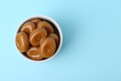 Photo of Tasty sweet caramel candies on light blue background, top view. Space for text