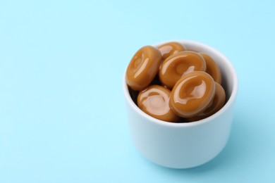 Photo of Tasty sweet caramel candies on light blue background, closeup. Space for text