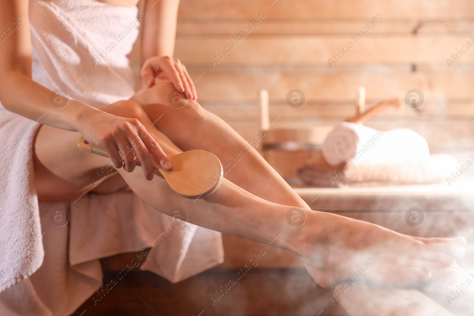 Woman massaging her leg with brush surrounded by steam in sauna, closeup Image of Woman massaging her leg with brush surrounded by steam in sauna, closeup