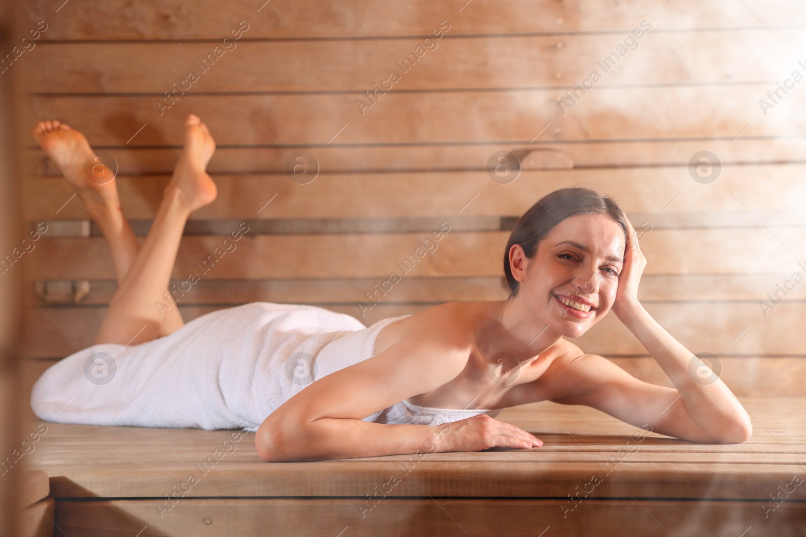 Smiling woman relaxing on bench surrounded by steam in sauna Image of Smiling woman relaxing on bench surrounded by steam in sauna