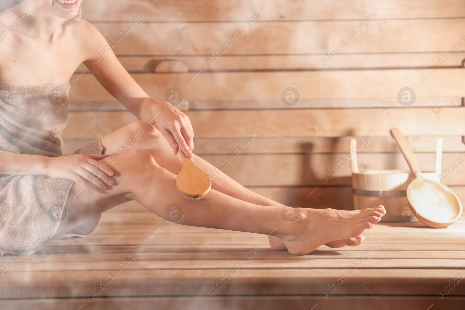 Woman massaging her leg with brush surrounded by steam in sauna, closeup Image of Woman massaging her leg with brush surrounded by steam in sauna, closeup