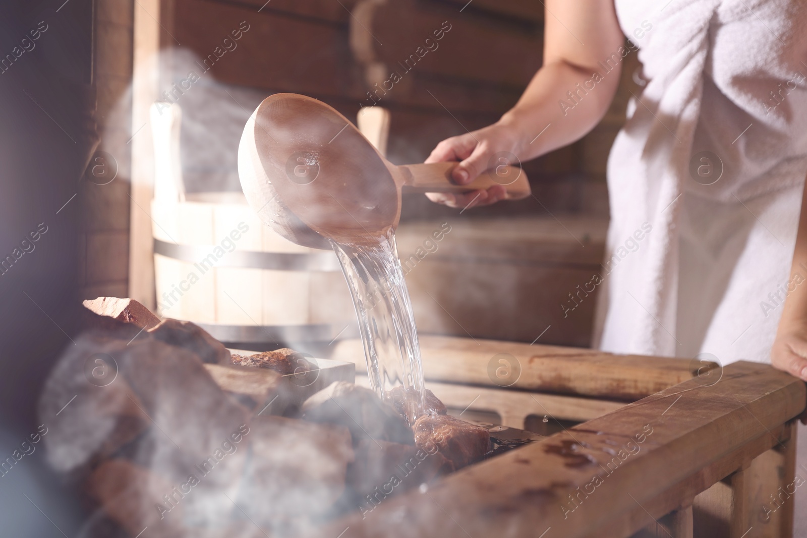 Woman pouring water onto stones surrounded by steam in sauna, closeup Image of Woman pouring water onto stones surrounded by steam in sauna, closeup