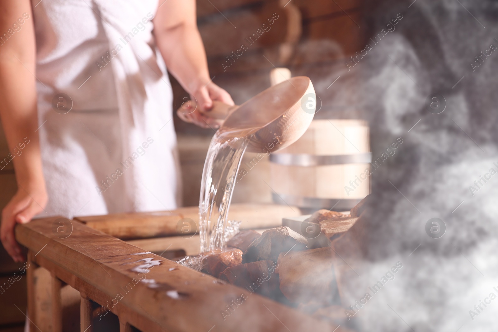 Woman pouring water onto stones surrounded by steam in sauna, closeup Image of Woman pouring water onto stones surrounded by steam in sauna, closeup